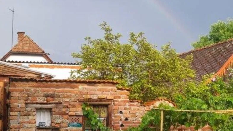 Idyllischer Gartenbereich mit Ziegelmauer, Sitzgelegenheit und einem Regenbogen am Himmel.