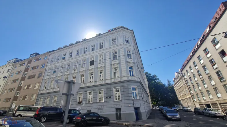 Mehrstöckiges Eckgebäude mit klassischer Architektur und vielen Fenstern an einem sonnigen Tag.