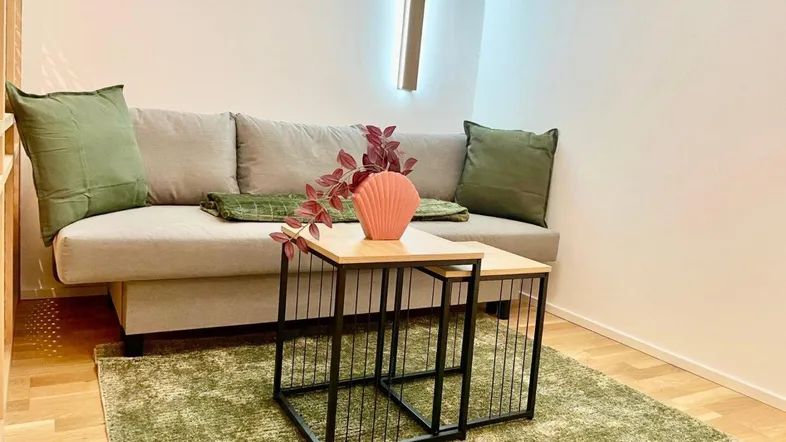Modernes Wohnzimmer mit beigem Sofa, grünem Teppich und stilvollen Beistelltischen.
