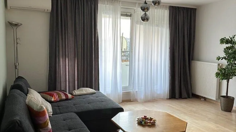 Gemütliches Wohnzimmer mit großem Ecksofa, Couchtisch und direktem Balkonzugang.
