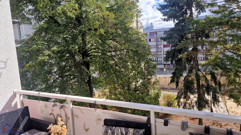 Blick vom Balkon mit grünen Bäumen und urbaner Umgebung. Gemütliche Sitzgelegenheiten laden zum Entspannen ein.