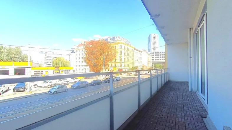 Heller Balkon mit Holzboden und Blick auf die belebte Stadtstraße und umliegende Gebäude.