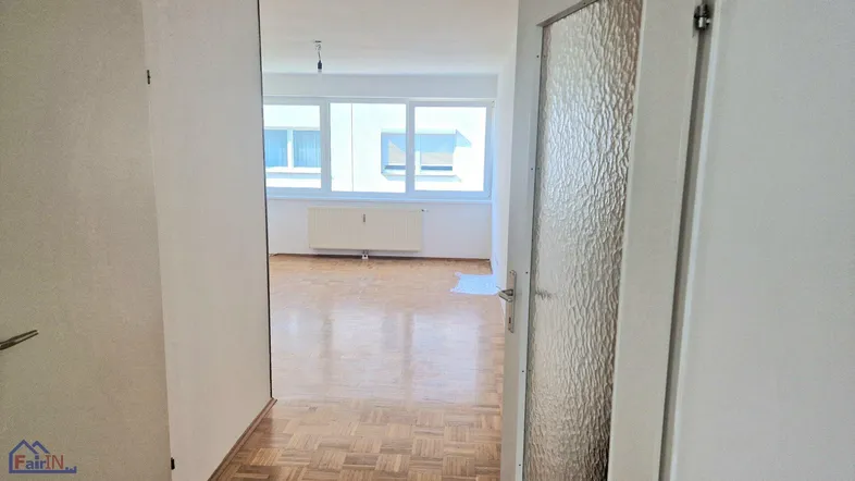 Heller Eingangsbereich mit Parkettboden, der in ein geräumiges Zimmer mit großen Fenstern führt.