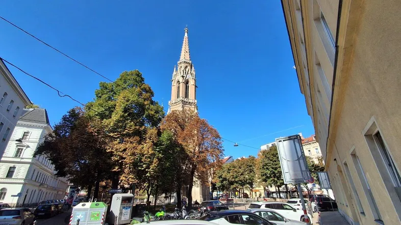 Stadtansicht mit historischer Kirche und geparkten Autos unter blauem Himmel.