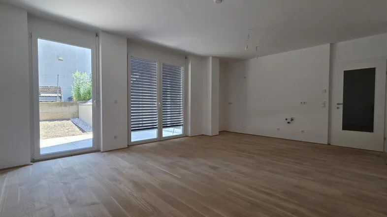 Helles, leeres Wohnzimmer mit neuem Parkettboden und Zugang zu einer Terrasse.