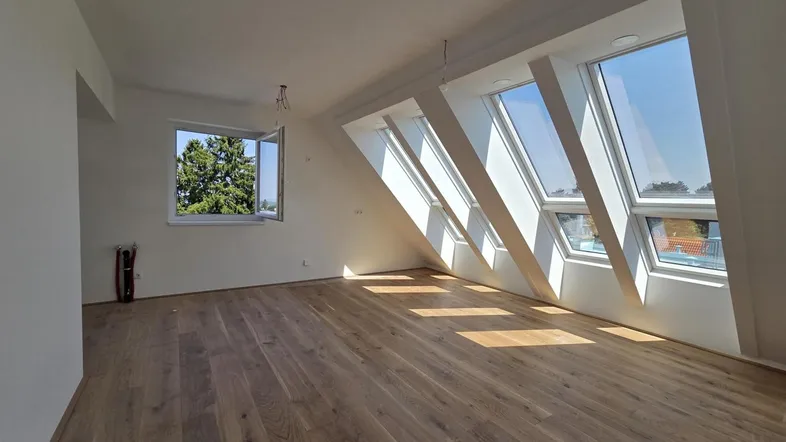Helles Dachgeschosszimmer mit Holzboden und mehreren Dachfenstern, die viel Tageslicht hereinlassen.