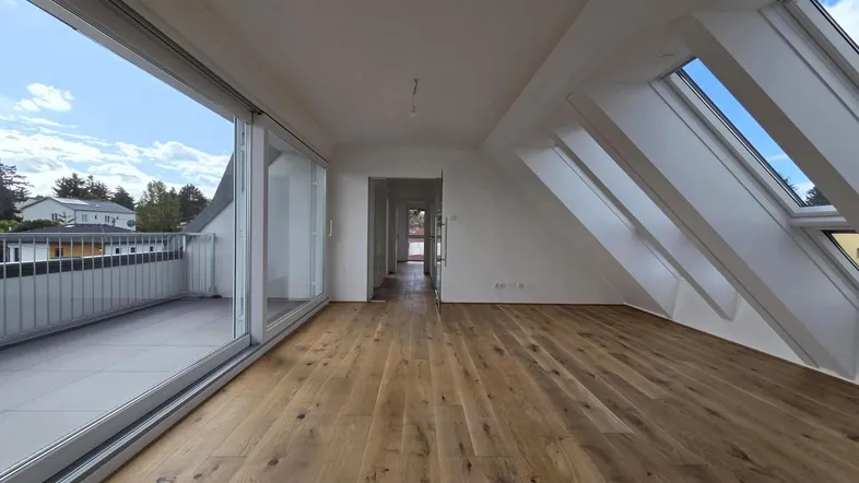 Heller Raum mit Holzboden, großen Schiebetüren zum Balkon und Dachfenstern für viel Tageslicht.