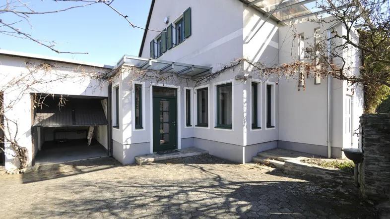 Vorderansicht des Hauses mit integrierter Garage und gepflasterter Einfahrt unter klarem Himmel.