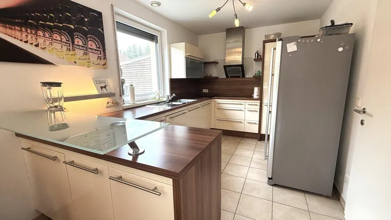 Moderne Küche mit beigefarbenen Schränken, Holz-Arbeitsplatten und einer praktischen Kücheninsel mit Glasplatte.