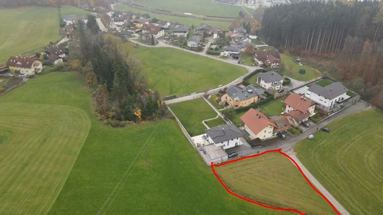 Luftaufnahme eines Wohngebiets mit grünen Feldern und einem markierten Baugrundstück in ländlicher Umgebung.