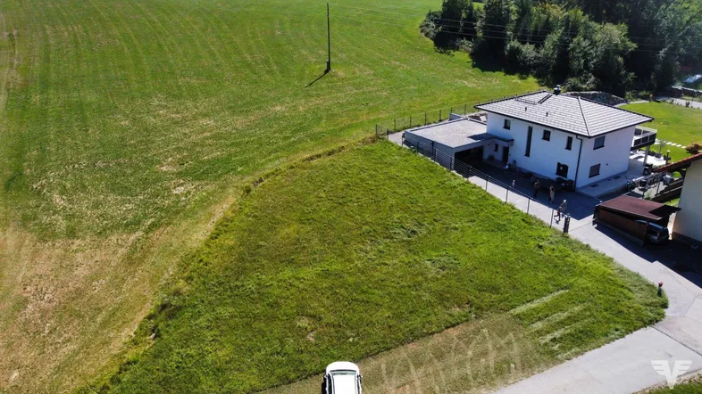 Luftaufnahme eines modernen Hauses mit Carport, umgeben von weitläufigen grünen Wiesen und Feldern.