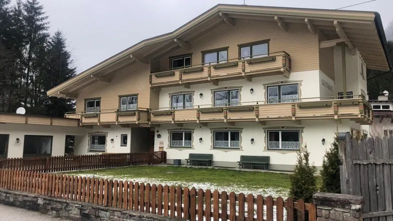 Traditionelles Gebäude mit mehreren Balkonen und Holzzaun im Vordergrund, umgeben von Natur.