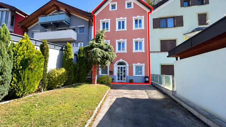 Mehrstöckiges Wohnhaus mit roter Fassade, umgeben von Grünflächen und einer Zufahrt.