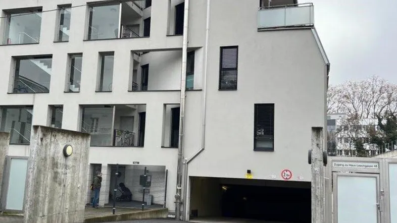 Moderne Gebäudefassade mit großen Fenstern, Balkonen und Zufahrt zur Tiefgarage.