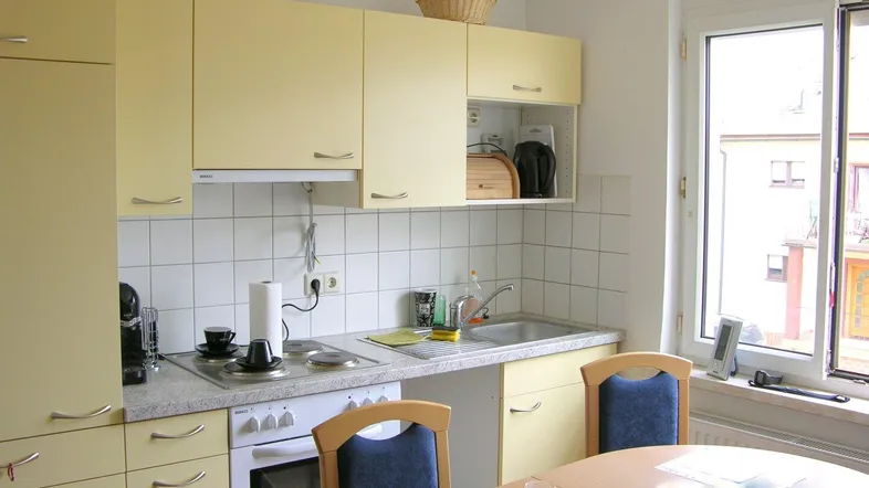 Helle Einbauküche in Gelb mit weißen Fliesen, Fenster und Essbereich.