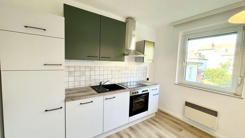 Moderne Einbauküche mit weißen und olivgrünen Schränken, ausgestattet mit Herd und Dunstabzugshaube.