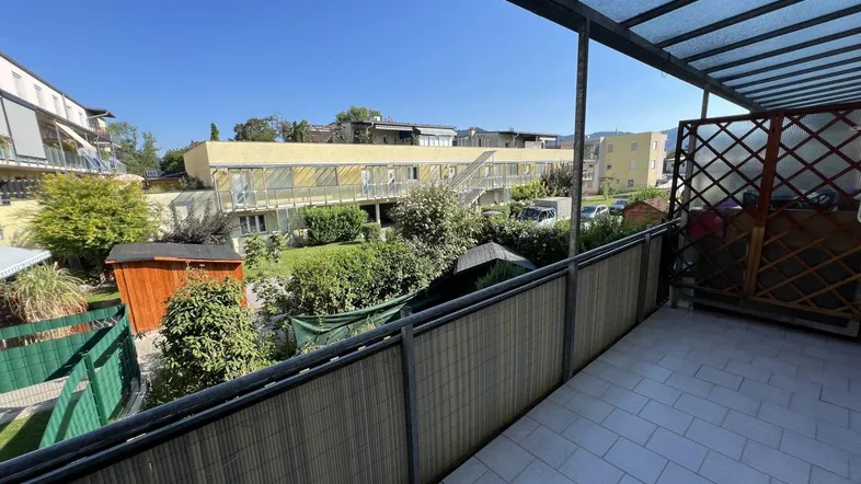 Überdachter Balkon mit Fliesenboden und Blick auf die umliegenden Gärten und Gebäude.