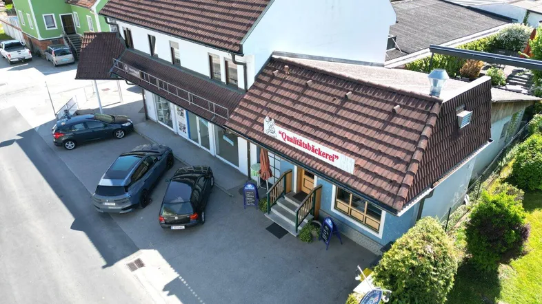 Luftaufnahme des Gebäudes mit Bäckerei-Café im Erdgeschoss und Parkplätzen davor.