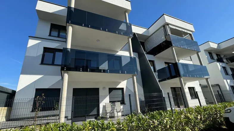 Moderne Wohnanlage mit weißer Fassade und Balkonen mit Glasbrüstung unter blauem Himmel.