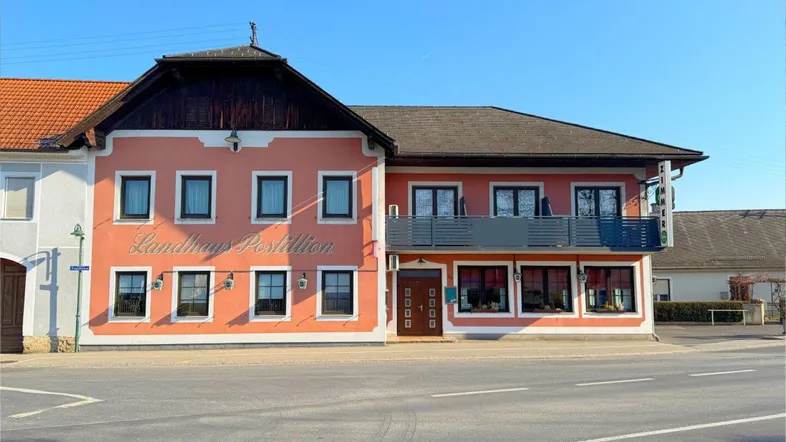 Traditionelles Landhaus mit rosafarbener Fassade und dunklen Fensterrahmen an einer Straße gelegen.