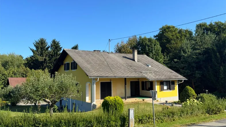 Gelbes Einfamilienhaus mit Satteldach und grüner Umgebung unter blauem Himmel.