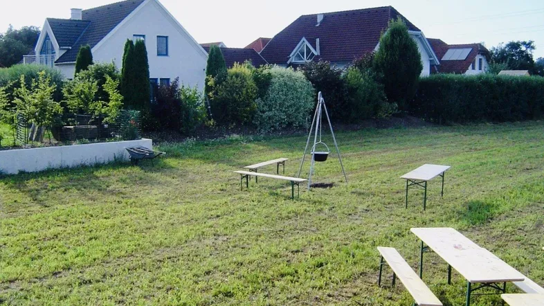 Große Rasenfläche mit Picknicktischen und Feuerstelle, umgeben von Wohnhäusern.