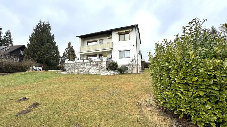 Das Haus von außen mit großem Rasenbereich und Bäumen, umgeben von Natur.