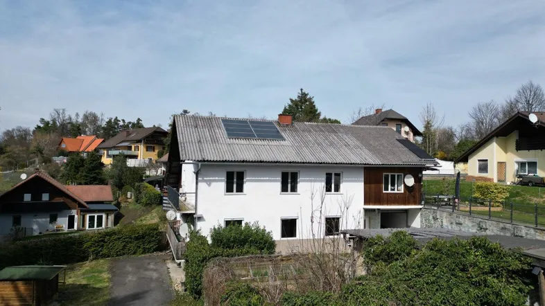 Weißes Wohnhaus mit Satteldach und Solaranlage in ländlicher Umgebung unter blauem Himmel.