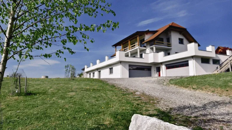 Großzügiges Anwesen mit modernem Haus, weitläufiger Grünfläche und Zufahrt unter blauem Himmel.