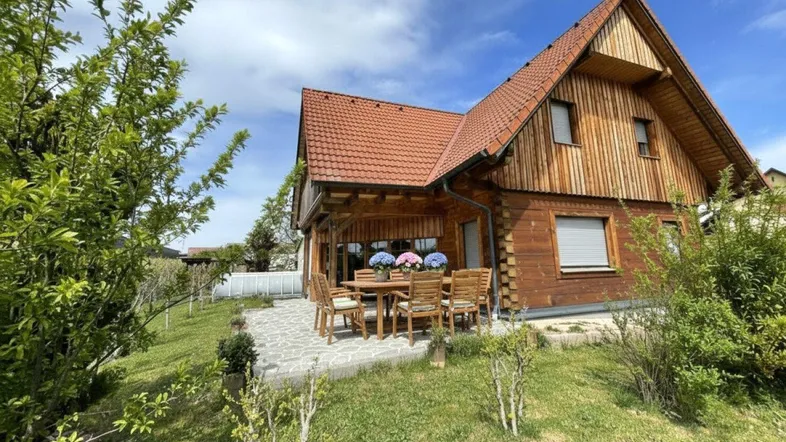 Gemütliche Terrasse mit Holztisch und Stühlen vor dem charmanten Holzhaus mit Ziegeldach.