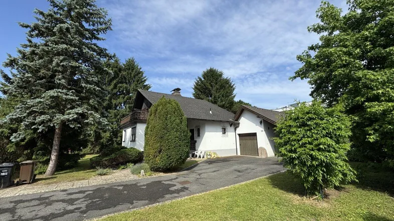Einfamilienhaus mit Auffahrt, Garage und umgebendem Grün unter strahlend blauem Himmel.