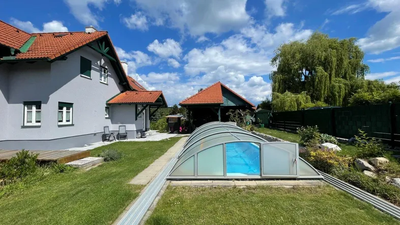 Großer Gartenbereich mit Rasenfläche, überdachtem Pool und Blick auf das Haus.