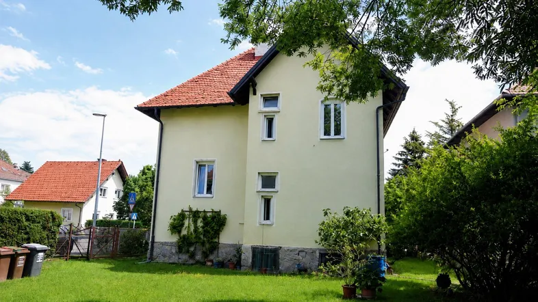 Ansicht eines Einfamilienhauses mit hellgelber Fassade, rotem Ziegeldach und gepflegtem Garten.
