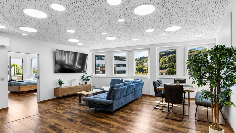 Helles Wohn- und Esszimmer mit modernem Sofa, Holzboden und weitem Blick ins Grüne.