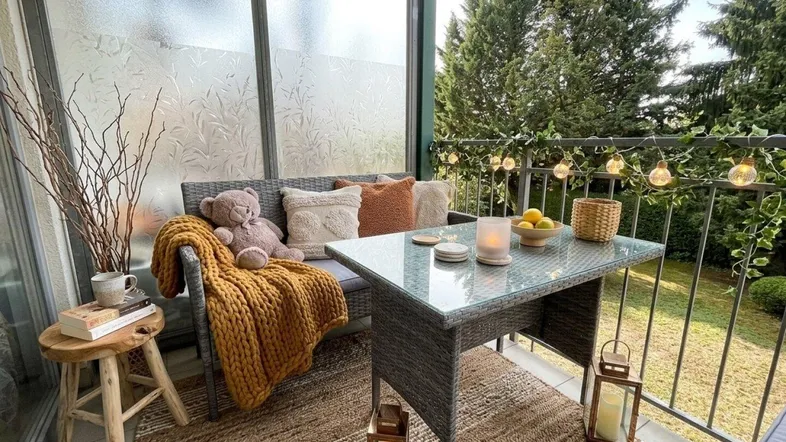 Gemütlicher Balkon mit Rattanmöbeln, Dekoration und Blick ins Grüne.