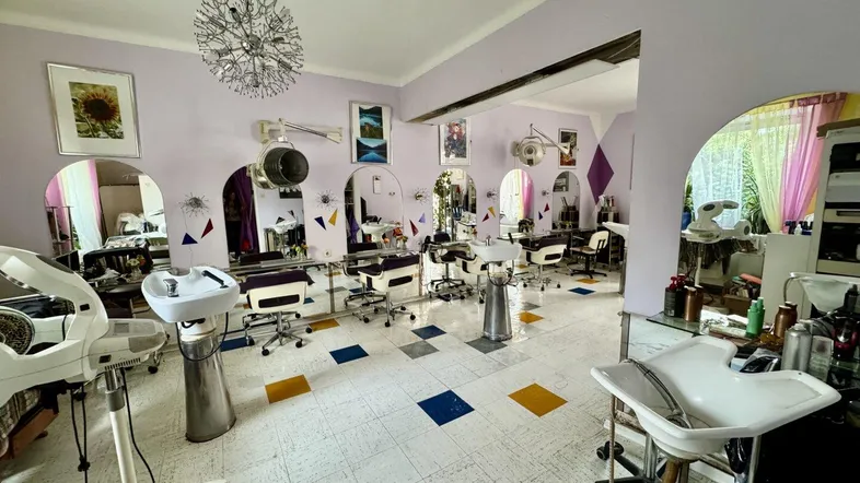 Geräumiger Friseursalon mit mehreren Styling-Stationen, Waschbecken und Fliesenboden in Lila und Weiß.