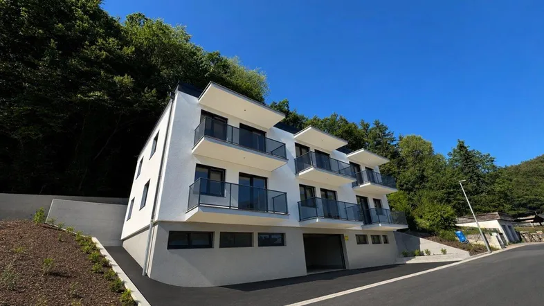 Modernes Mehrfamilienhaus mit Balkonen und Tiefgaragenzufahrt, eingebettet in eine grüne Hanglage.
