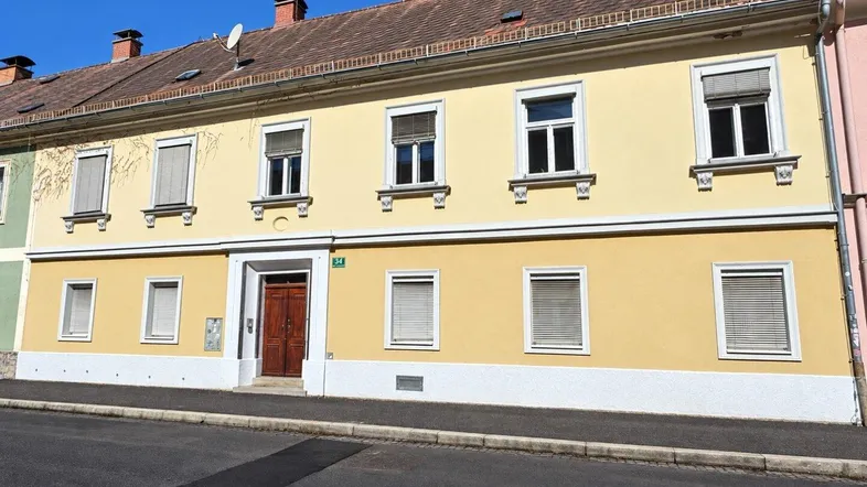 Gelbe Fassade eines Mehrfamilienhauses mit mehreren Fenstern und Rollläden an einem sonnigen Tag.