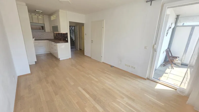 Helles Wohnzimmer mit Parkettboden und Zugang zu einem Balkon, offen zur Küche.