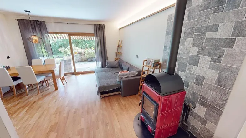 Geräumiger Wohn-Essbereich mit Holzboden, gemütlichem Sofa und einem traditionellen Kaminofen.
