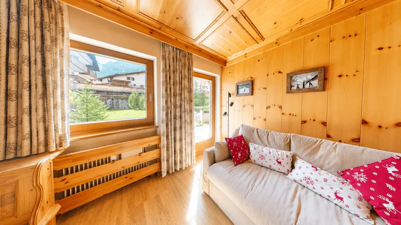 Gemütliches Wohnzimmer mit viel Holz, beiger Couch und Blick ins Grüne.