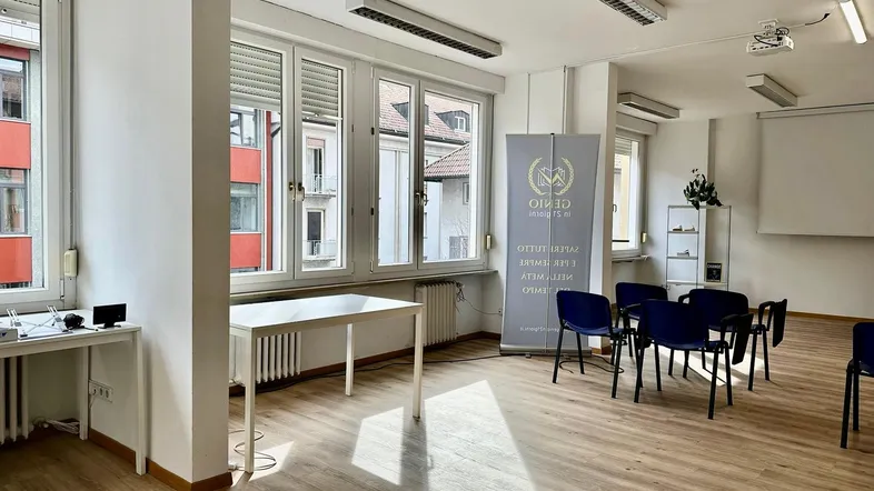 Heller Büroraum mit großen Fenstern, Holzfußboden und Präsentationsbereich für Schulungen.