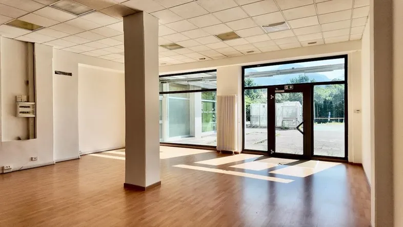 Geräumiger, leerer Raum mit Holzfußboden und großen Glasfenstern, ideal für Büro oder Gewerbe.