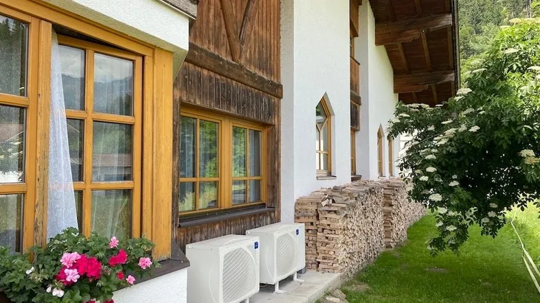 Traditionelle Fassade mit Holzelementen, Blumenkästen und modernen Außengeräten für die Heizung.