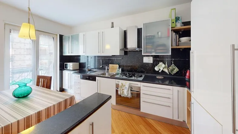 Moderne Küche mit weißen Schränken, dunkler Arbeitsplatte und Essbereich mit Holzboden.