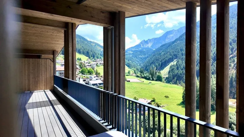 Geräumiger Balkon mit Holzboden und atemberaubendem Blick auf die umliegende Berglandschaft und das Tal.