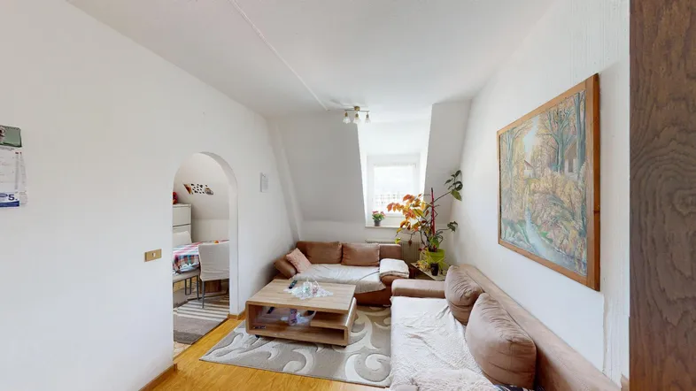 Gemütliches Wohnzimmer mit Dachschrägen, bequemen Sofas und einem Durchgang zum Essbereich.