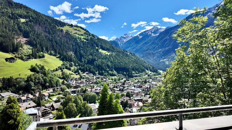 Panoramablick auf ein malerisches Tal mit einem Dorf und majestätischen Bergen unter blauem Himmel.