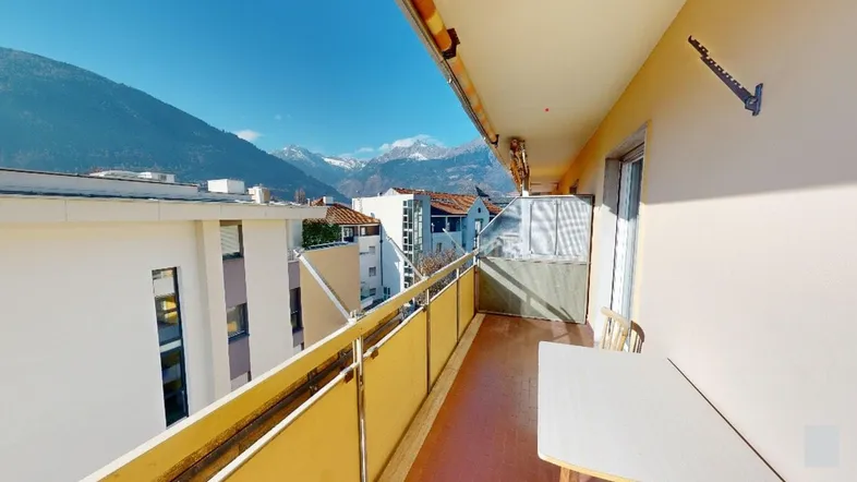 Sonniger Balkon mit Bergblick und umliegenden Gebäuden.