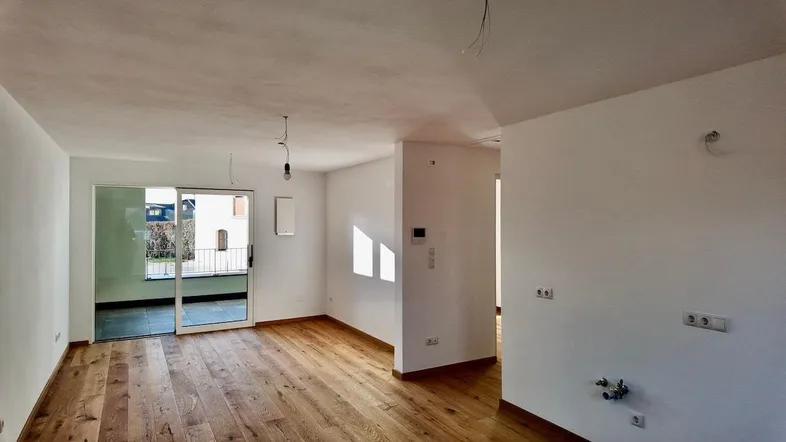Heller Wohnbereich mit neuem Parkettboden und Zugang zu einem Balkon, bereit für die Einrichtung.